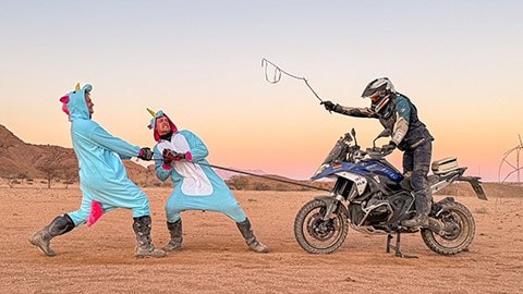 Two riders on the German men’s team in unicorn costumes pulling on a tow rope, which is attached to an R 1300 GS. The third rider sits on the motorcycle, cracking a whip.